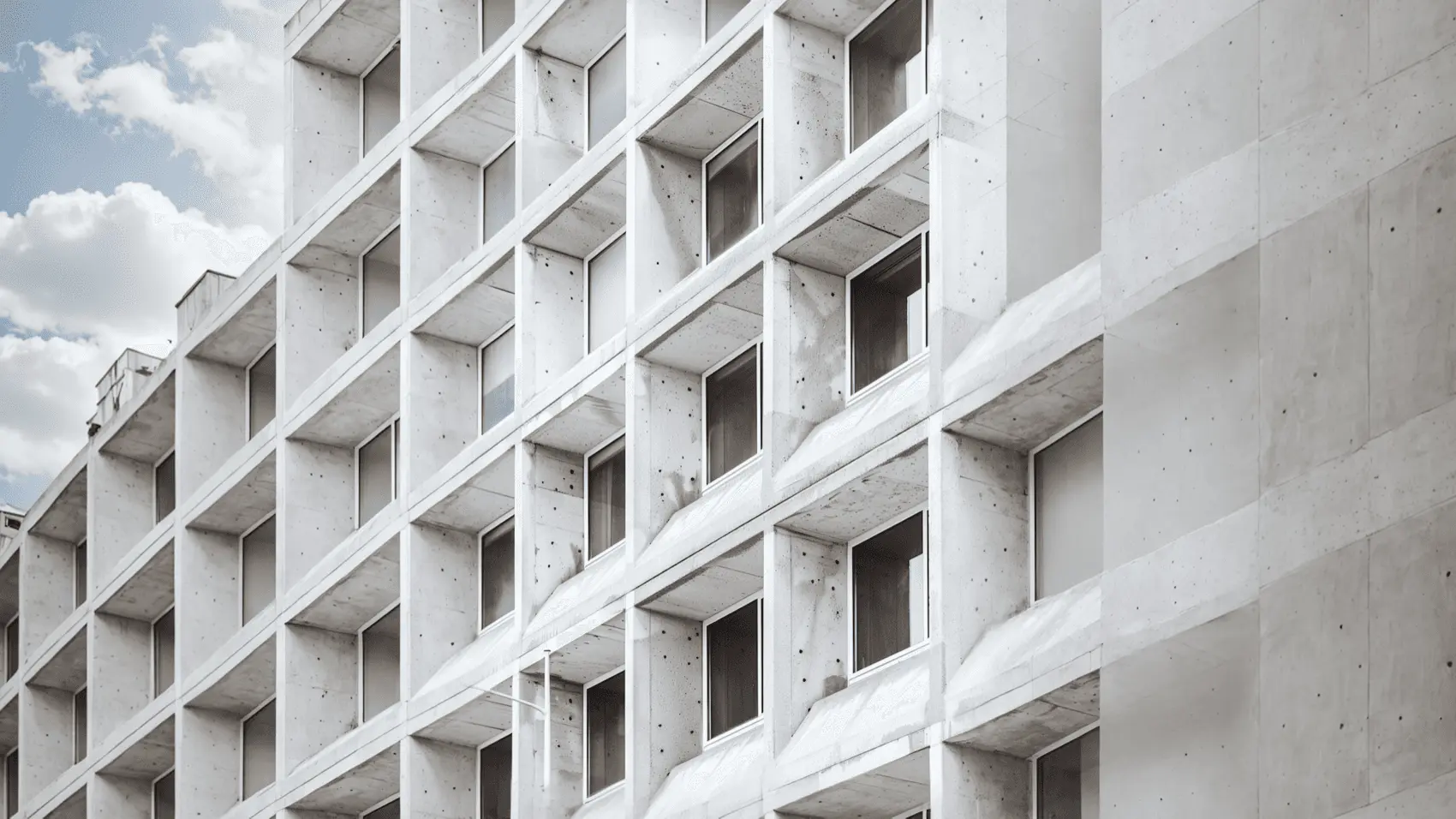A white concrete facade of deep, repeating window bays under a cloudy sky