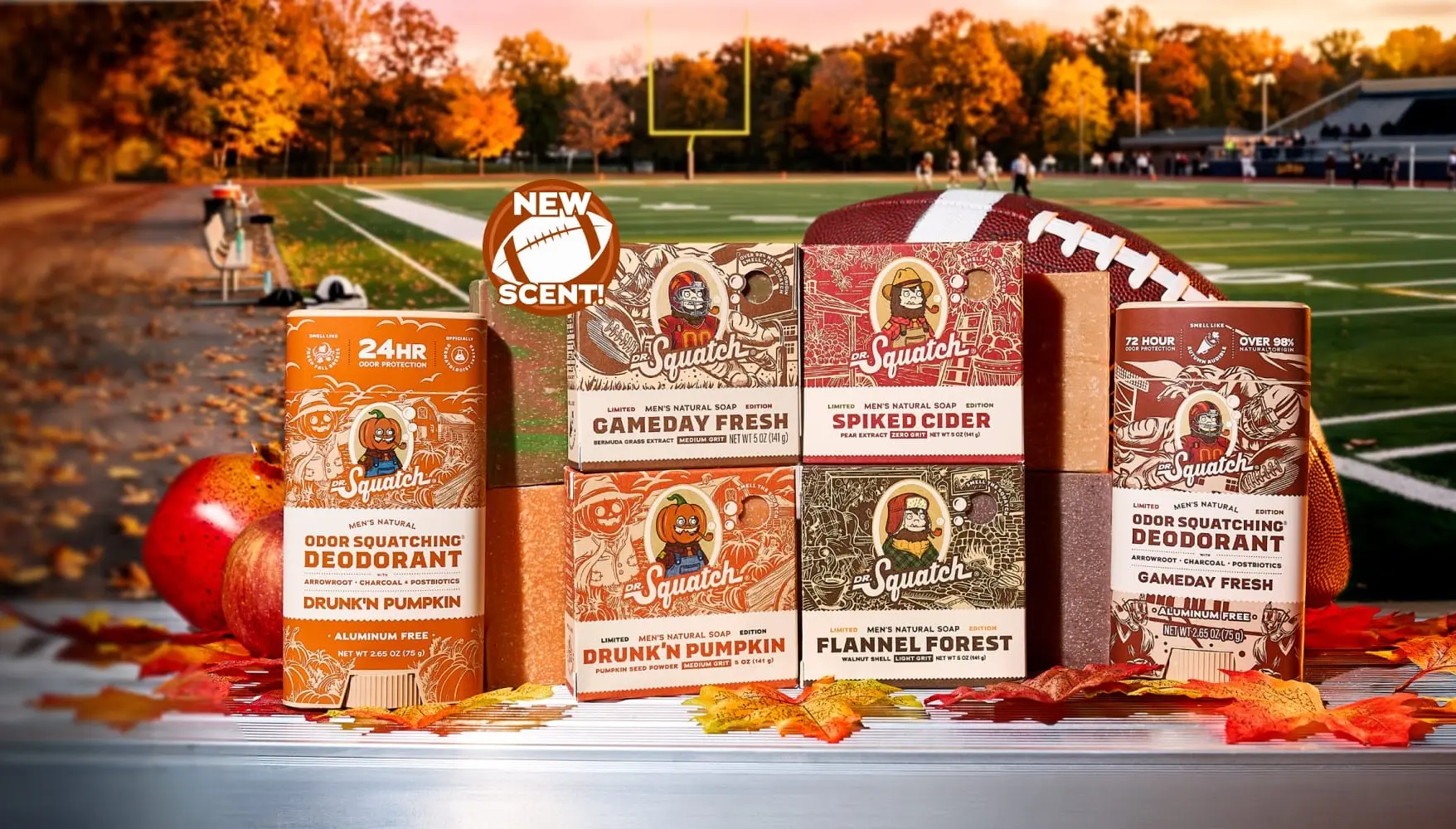 Dr. Squatch bar soaps and deodorants in autumn editions, stacked on a bench beside a football, with a playing field and orange trees behind