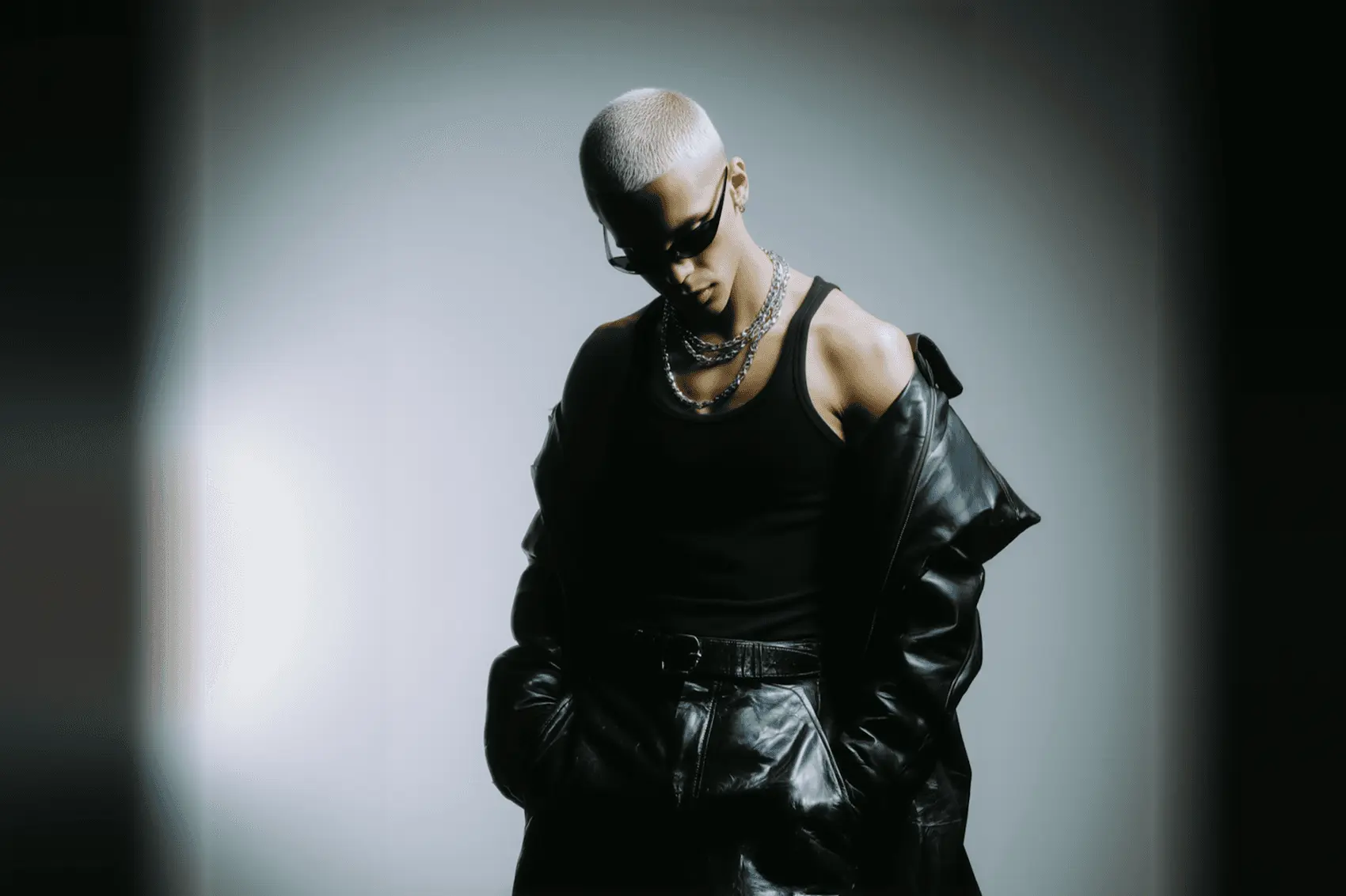 A man in sunglasses and a black leather coat against a pale backdrop